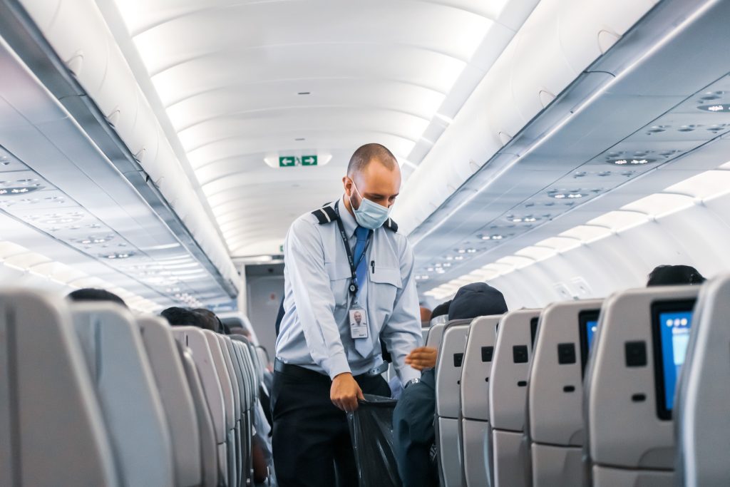 male-flight-attendant-on-the-aisle-collecting-trash-from-passenger